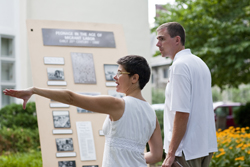 Noelle Damico, while standing beside a man, points with her left hand.